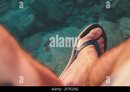 En regardant vers le bas vers les pieds masculines portant des sandales ou des flipflops au-dessus de l'eau de mer. Au-dessus de la vue des tongs sur les pieds d'homme au-dessus de l'eau. Banque D'Images