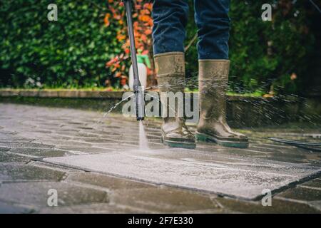 Personne nettoyant un tapis ou un tapis de sol à l'aide d'un nettoyeur haute pression. Nettoyer les tapis avec un jet haute pression tout en portant des bottes en plastique Banque D'Images