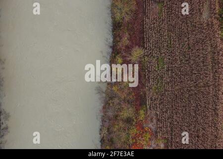 Vue aérienne de la rivière sombre blanche et des champs à côté. Photo à l'envers d'une rivière et de champs en automne, jour gris terne. Banque D'Images