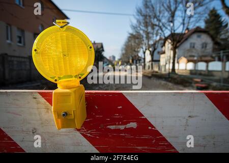 Une barrière lumineuse ou une lanterne jaune est montée sur une barrière ou un bloc rouge et blanc devant un chantier de construction. Bloc de route avec barrière et yello Banque D'Images