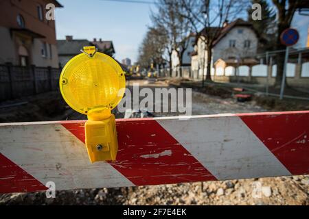 Une barrière lumineuse ou une lanterne jaune est montée sur une barrière ou un bloc rouge et blanc devant un chantier de construction. Bloc de route avec barrière et yello Banque D'Images