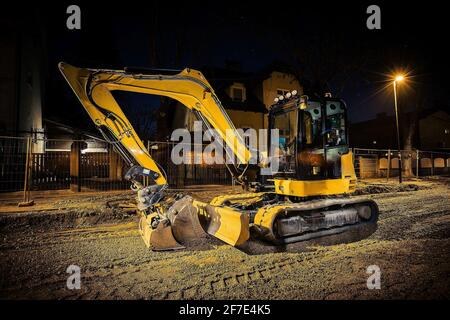 Chantier de construction sur une rue de la ville. Une excavatrice de creuseur jaune garée pendant la nuit sur un chantier de construction. Maisons en arrière-plan. Banque D'Images