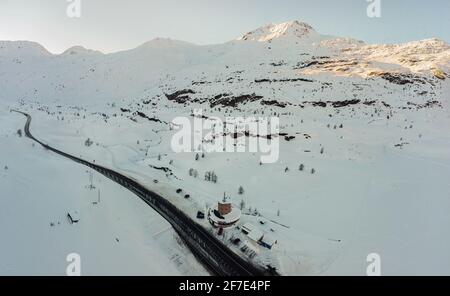 Photo de drone aérienne des maisons sur le dessus du col du simplon couvertes de neige hivernale. Maison entourée d'une grande quantité de neige avec des montagnes visibles Banque D'Images