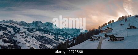 Fermes et cottages isolés sur la pente au-dessus de la vallée d'Adelboden et d'Engstligen, en début de soirée en hiver. De la neige est visible sur le maj Banque D'Images