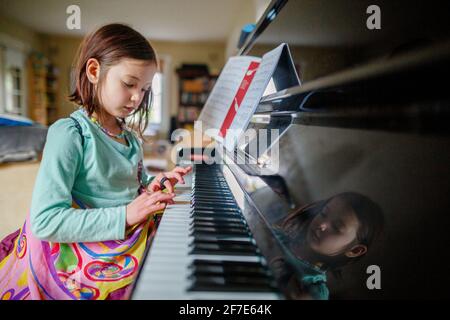 Une petite fille dans des ailes de papillon est assis à jouer au piano musique à l'intérieur Banque D'Images