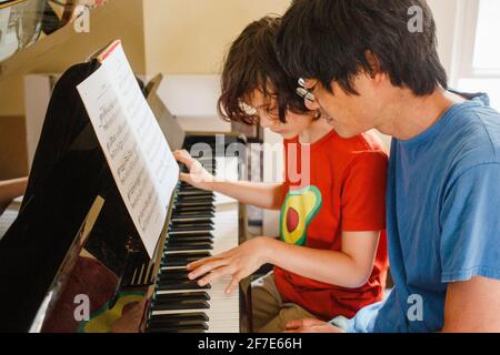 Un garçon et un père s'assoient ensemble pour jouer du piano musique à la maison Banque D'Images