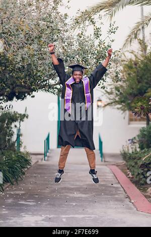 Homme excité d'être diplômé de l'université, portant une robe de graduation / chapeau. Banque D'Images