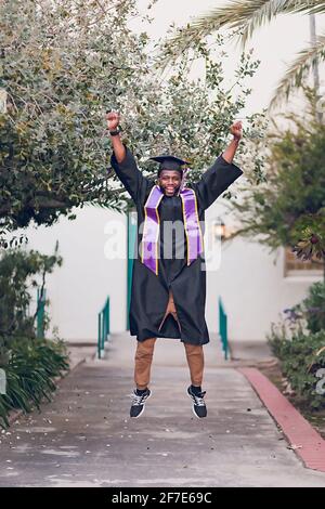 Homme excité d'être diplômé de l'université, portant une robe de graduation / chapeau. Banque D'Images