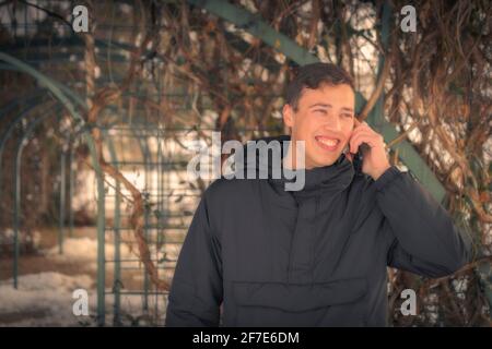 Un jeune garçon d'université aux yeux bleus souriant tout en parlant sur un téléphone portable à jardin Banque D'Images