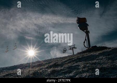 Silhouette d'un canon à neige ou d'une machine à neige artificielle sur une piste de ski par une journée ensoleillée. Lumière solaire visible derrière l'échappement d'un canon Banque D'Images