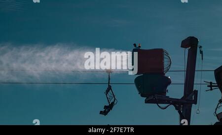 Silhouette d'un canon à neige ou d'une machine à neige artificielle sur une piste de ski par une journée ensoleillée. Lumière solaire visible derrière l'échappement d'un canon Banque D'Images