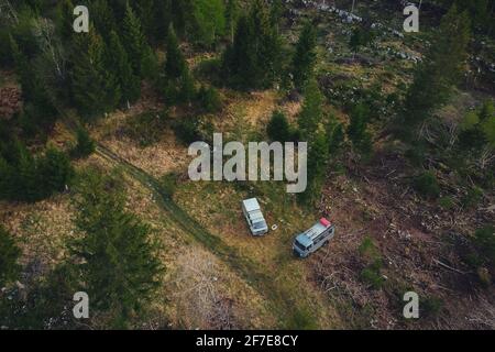 Deux anciens véhicules de camping-cars vintage faits sur mesure garés le matin dans la plaine forestière. Vue sur les drones de la nuit aventureuse avec une voiture Banque D'Images