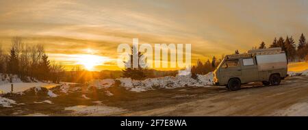 Véhicule d'aventure d'époque ou camping-car stationné dans la neige avec des chaînes à neige montées sur les roues arrière. Le lever du soleil est visible en arrière-plan. Banque D'Images