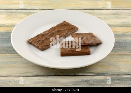 Barre de bonbons de caramel d'amande recouverte de chocolat au lait riche et des morceaux sur l'assiette à collation blanche Banque D'Images