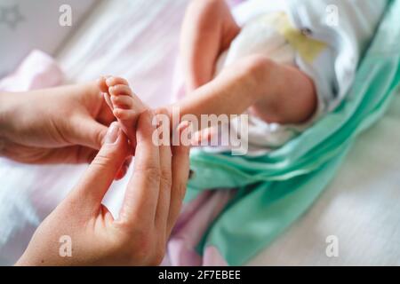 Gros plan sur la main de la femme caucasienne inconnue mère tenir le pied de son bébé bébé enfant massage doux sur le lit à la maison - la maternité et l'alter de personnes réelles Banque D'Images