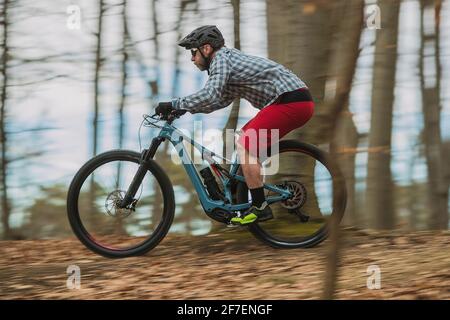 Un motard hippster se recharge en descente avec un vélo électrique léger ou un VTT moderne en automne ou en hiver dans une forêt. Banque D'Images