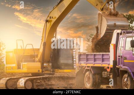 Pelle rétro travaillant en creusant le sol sur le chantier et en le chargeant sur le tombereau. Le godet de la pelle rétro transporte le sol vers le camion. La pelle sur chenilles décharge la saleté Banque D'Images