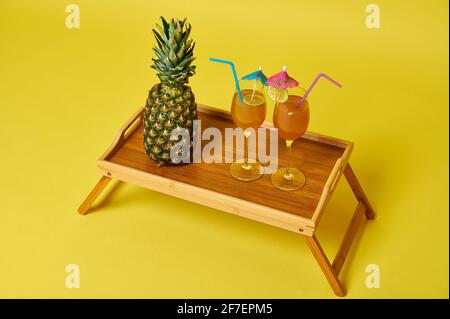 Vue en grand angle du plateau en bois avec plats et boissons. Ananas et deux verres avec cocktails exotiques d'été décorés avec un parasol Banque D'Images