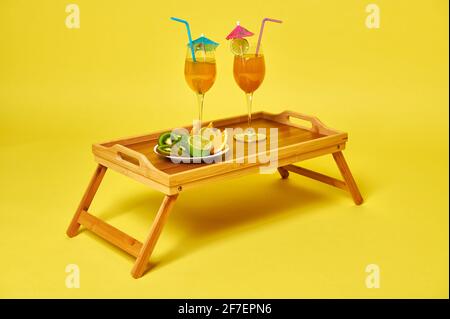 Deux verres avec cocktails exotiques d'été décorés avec un parasol et une assiette de fruits en tranches sur un plateau de service en bambou. Concept de nourriture et de boissons Banque D'Images