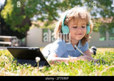 Un petit élève utilise un ordinateur portable ou une tablette et écrit du nomwork dans le parc scolaire. Enfant scolaire en bonne santé. Banque D'Images