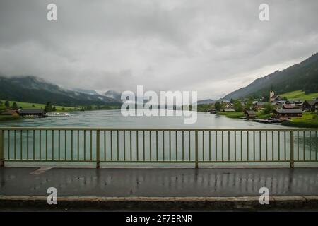 Pont avec balustrade métallique verte sur le lac de Weissensee en Autriche par un jour très nuageux et pluvieux. Banque D'Images