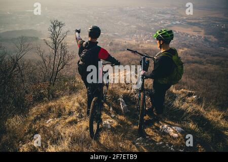 Deux hommes avec des monttaibikes sur un sommet de la colline. Panorama d'une vallée avec cycliste dans l'avant-groupe. On pointe son fingeer. Banque D'Images