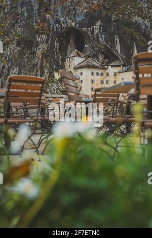 Sièges, tables et fleurs devant le château de Predjama, une magnifique forteresse construite dans une face rocheuse. Concept de détente et de vue pour touris Banque D'Images