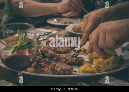 Les mains d'une personne ont vu couper des morceaux de viande fraîche cuite ou cuite dans un restaurant. Verre visible de vin et de pomme de terre. Un moment festif dans un restaurant Banque D'Images