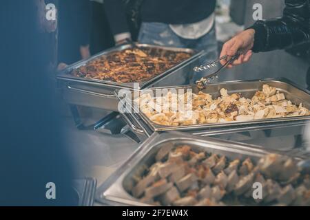 Des mains de personnes ont vu prendre de la nourriture dans des conteneurs en acier inoxydable lors d'un buffet ou d'un gala de restauration. Une cuisine savoureuse est servie lors d'un événement de restauration. Banque D'Images