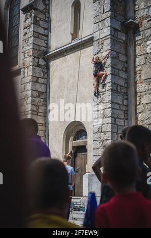 Jeune femme grimpant sur le mur d'une église. Athlète grimpant sur un clocher de l'église dans le cadre d'une exposition. Les gens qui la regardent grimper Banque D'Images