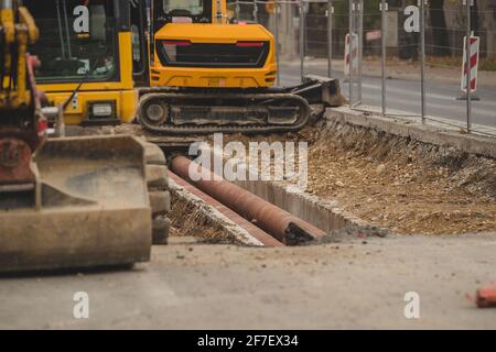 Remplacement des tuyaux ou des tuyaux sous la surface de la route. Des tuyaux visibles sous la chaussée, entourés par des pelles rétro ou des excavateurs qui déplacent la terre. Banque D'Images