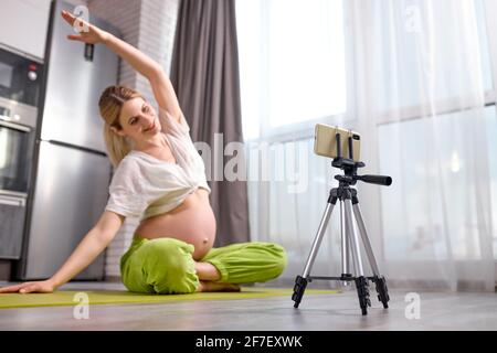 Femme enceinte pratiquant le yoga à la maison avec un smartphone. Femme enceinte faisant la formation prénatale de vidéo. Femme méditer pendant la grossesse. En ligne Banque D'Images