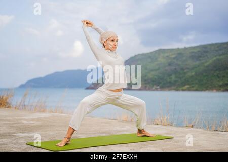 Kundalini yoga femme en vêtements blancs et turban pratique le yoga kundalini sur le fond de la mer, des montagnes et du coucher du soleil. Peinture de visage de combat Banque D'Images