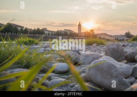 Vue sur la basilique de San Zeno Maggiore à Vérone au coucher du soleil surplombant la rivière Adige avec des pierres et de l'herbe sur la rive de la rivière. Romantique picuture de Banque D'Images