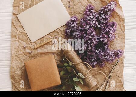 Carte élégante, belles fleurs lilas, cadeau, ciseaux vintage, crayon et ficelle sur fond rustique, vue du dessus. La vie rurale encore. Carte de vœux templa Banque D'Images