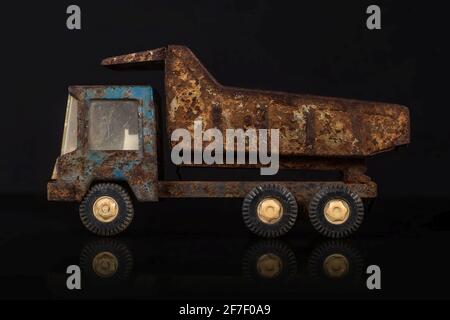 Côté d'un ancien modèle métallique en étain sale et très rouillé d'un camion à benne de couleur bleue et grise dans un fond noir et bleu sur une surface réfléchissante. Banque D'Images