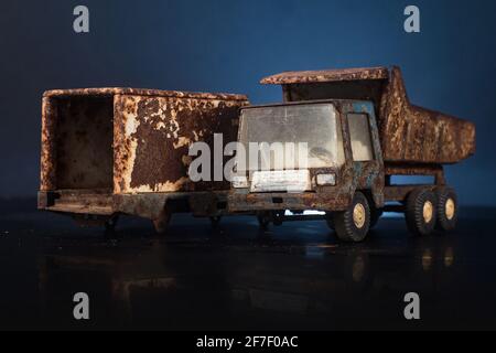 Paire de vieux, sale et très rouillé en métal d'étain modèles de jouets de camions de couleur bleue et grise dans un arrière-gorund noir et bleu sur la surface réfléchissante. Un petit-lait Banque D'Images