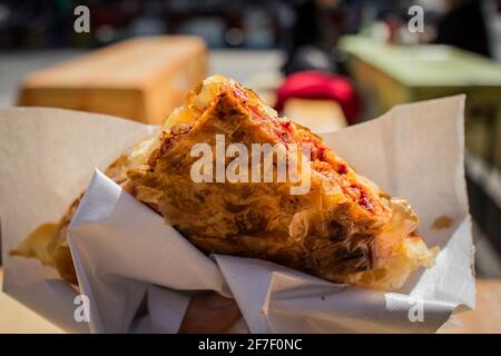 Personne tenant un morceau de burek à saveur de pizza, un repas traditionnel des balkans dans sa main à l'extérieur. En-cas rapide dans la ville. Banque D'Images