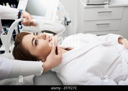 Femme caucasienne adulte lors de l'élimination des taches brunes sur le visage par TECHNOLOGIE DE rajeunissement ELOS à la clinique de cosmétologie Banque D'Images