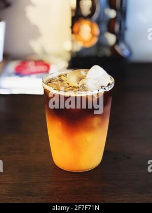 Café glacé à l'orange - UN verre en plastique d'americano mélangé avec du soda artisanal et du jus d'orange yuzu sur fond flou, boisson rafraîchissante conc d'été Banque D'Images