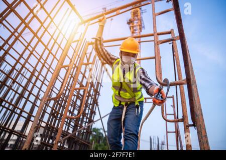 Travailleur asiatique travaillant en hauteur sur le chantier de construction. Dispositif antichute pour travailleur avec crochets pour harnais de sécurité sur la selle Banque D'Images