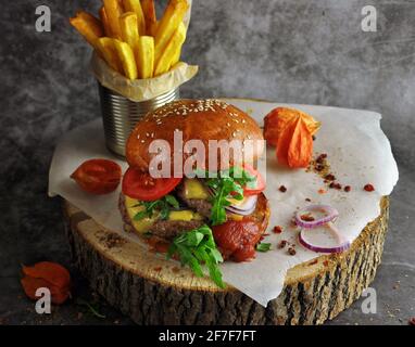 Hamburger sur un pain à grains entiers avec de la laitue et des pommes de terre grillées sur une planche de service en bois. Vue rapprochée Banque D'Images