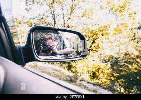 Selfie d'une fille dans la vue arrière de la voiture pendant que la voiture est en marche. La fille porte ses cheveux attachés et la souffle loin avec le vent. Banque D'Images