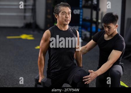 Homme mature s'entraîner avec un entraîneur personnel à la salle de gym Banque D'Images
