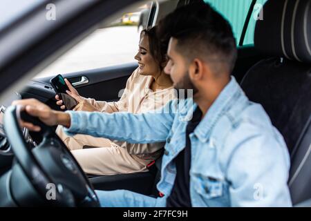 Une femme perplexe tient un smartphone, utilise des cartes en ligne, montre à son mari, essaie de trouver le chemin, est perdue dans la grande ville, voiture, voyage dans un pays étrange Banque D'Images