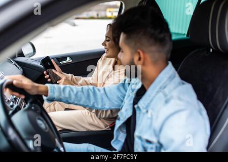 Une femme perplexe tient un smartphone, utilise des cartes en ligne, montre à son mari, essaie de trouver le chemin, est perdue dans la grande ville, voiture, voyage dans un pays étrange Banque D'Images