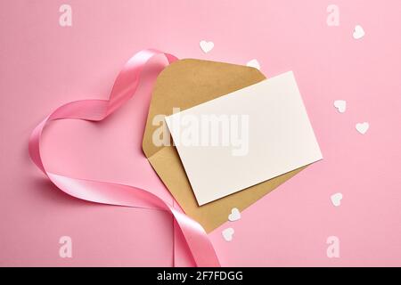 Maquette de carte de vœux avec ruban rose et coeurs en papier blanc. Invitation blanche vierge sur fond rose Banque D'Images