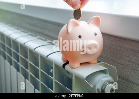 Le concept de payer pour le chauffage dans les maisons avec un climat froid. Porceuse de banque sur un radiateur en métal blanc. Le concept de l'économie sur les utilitaires Banque D'Images