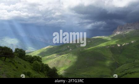 Nuages épais sur la chaîne de montagnes. Les rayons du soleil illuminent les prairies. Paysage panoramique. Ton. Banque D'Images