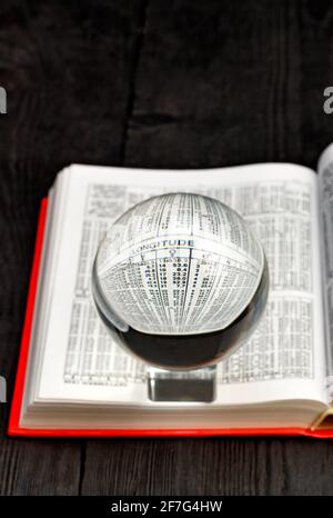 Une boule de cristal se dresse sur un livre ouvert d'éphémérides dans une couverture rouge vif sur fond d'une table en bois noir. Image verticale, espace de copie. Banque D'Images